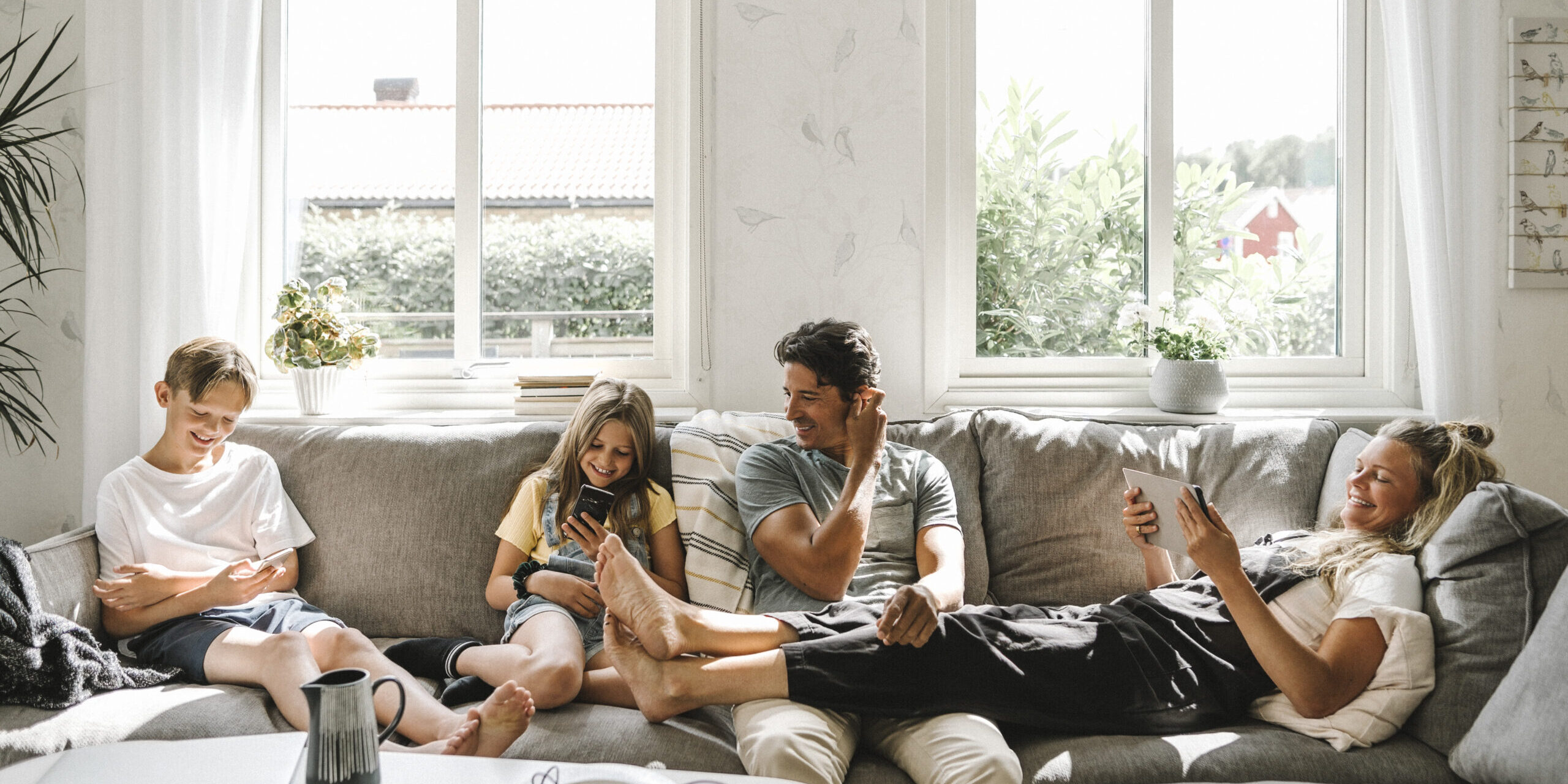 Happy family sitting on sofa in living room Remplacer une baie vitrée