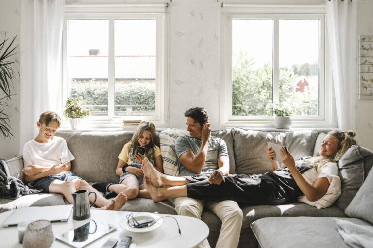 Happy family sitting on sofa in living room Remplacer une baie vitrée